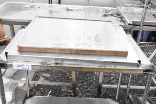 Metal table with under shelf, stainless steel, used condition, visible wear and grime. Label indicates "235 Metal Table".