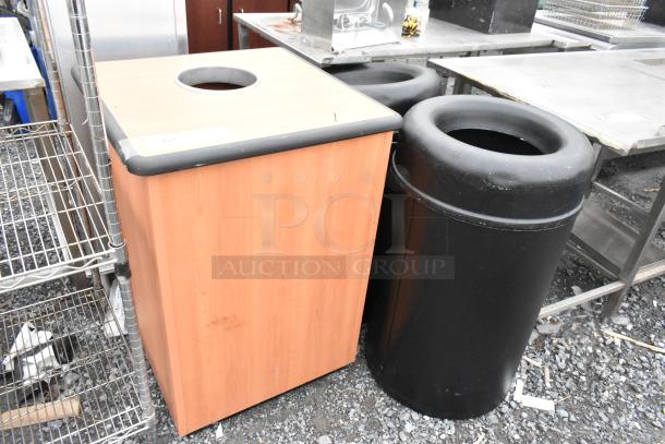 3 trash can shells; 2 black cylindrical, 1 wood-patterned square. Used condition, outdoor setting.
