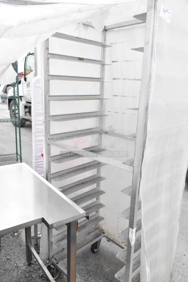 Metal commercial pan transport rack with several shelves, on sturdy commercial casters, covered with a white protective cover.