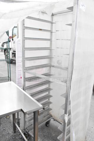 Metal commercial pan transport rack with several shelves, on sturdy commercial casters, covered with a white protective cover.