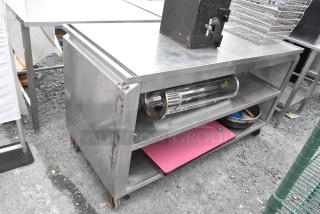 Stainless steel table with under shelves, visible rust, on commercial casters. Includes contents like trays and a pink mat.