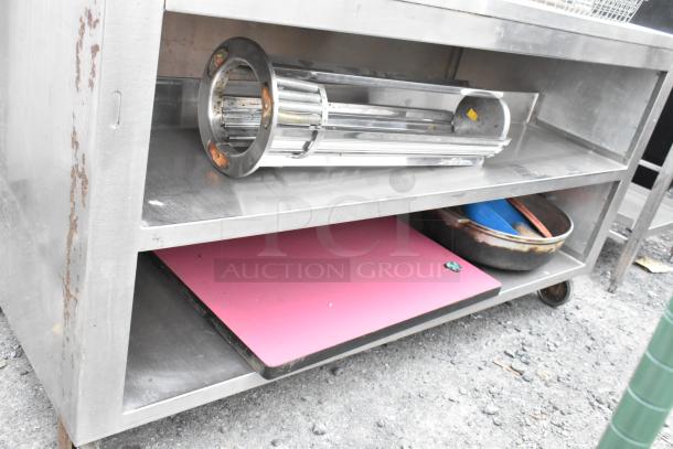 Stainless steel table with two under shelves, rusty spots, commercial casters, includes metal cylinder and pink cutting board.