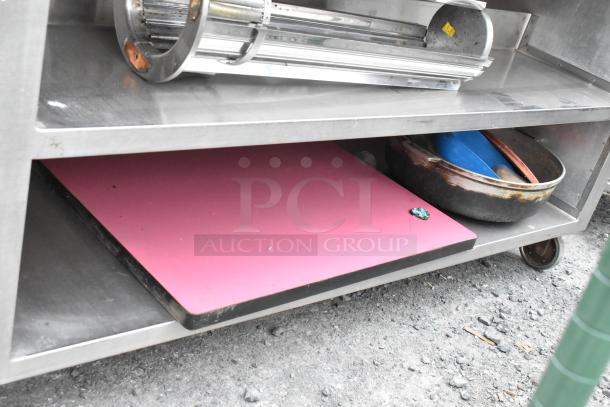 Stainless steel table with under shelves, two-tier storage, on commercial casters. Includes various kitchen items. Good condition.