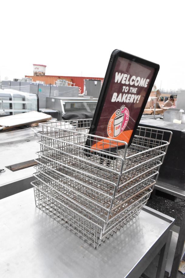 Stainless steel table with under shelves on commercial casters, contains stacked wire baskets and a "Welcome to the Bakery!" sign.