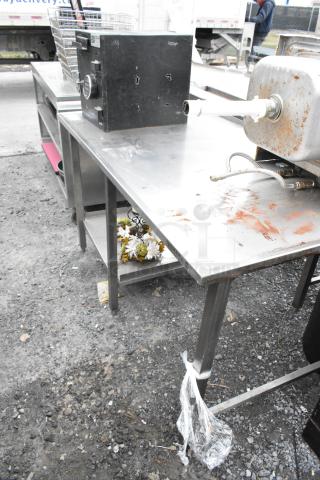 Stainless steel table with shelf, showing surface rust and wear, sturdy legs, suitable for kitchen or workshop use.