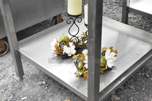 Stainless steel table with a lower shelf, decorative flower and candle arrangement, in good condition.