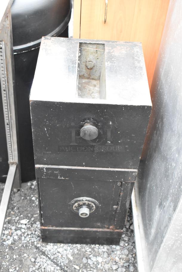 Black metal single compartment safe with visible dial lock, no combination included, signs of wear evident.