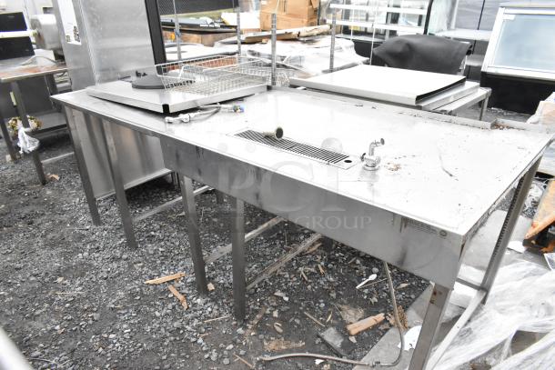 Stainless steel table with built-in faucet and drain, commercial use, visible wear, Horacios Inc. label on side.