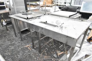 Stainless steel table with built-in faucet and drain, commercial use, visible wear, Horacios Inc. label on side.