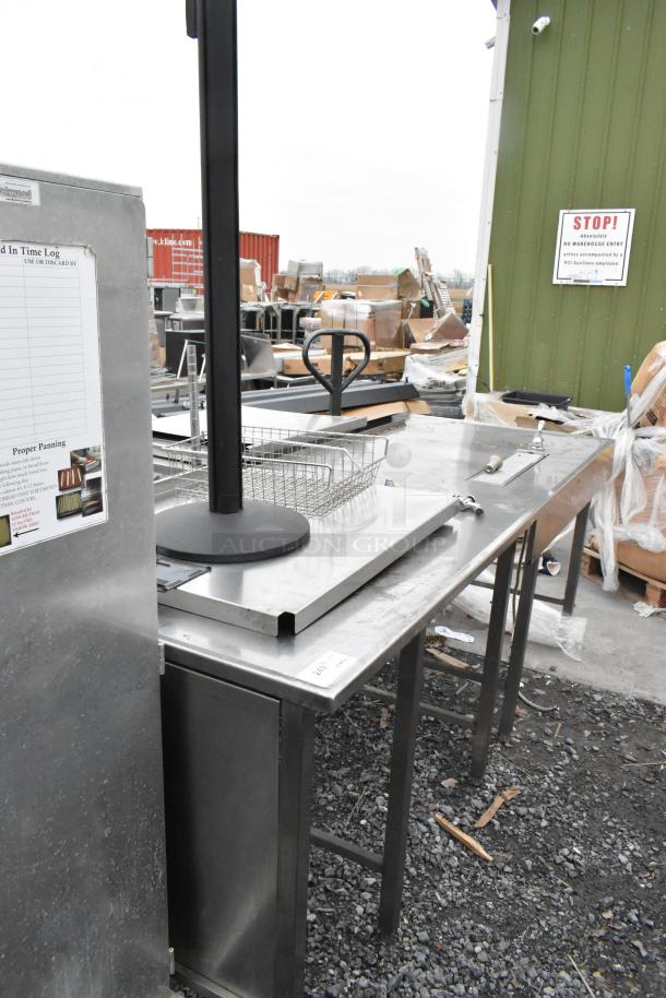 Stainless steel table, sturdy design, slight wear. Includes a side compartment and open shelving. Ideal for commercial use.