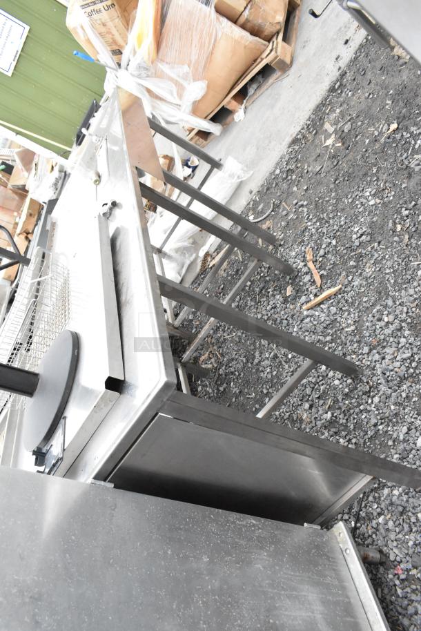 Stainless steel table with sturdy legs, featuring a smooth surface and a side basket. In used condition.