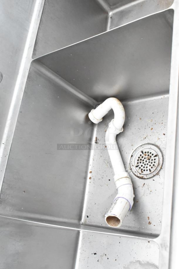 Stainless Steel 3 Bay Sink with dual drain boards, visible piping, and minor wear; ideal for commercial use.