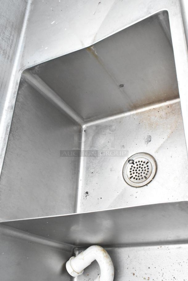 Stainless steel 3 bay sink with dual drain boards, visible plumbing, some wear. Ideal for commercial use.