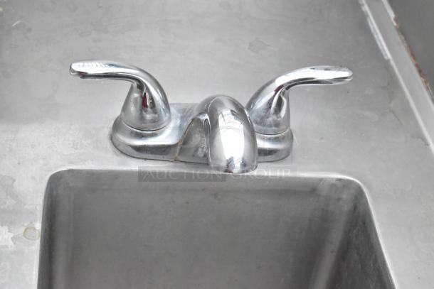 Stainless steel single bay sink with faucet, dual handles, and splash guards, showing moderate wear.