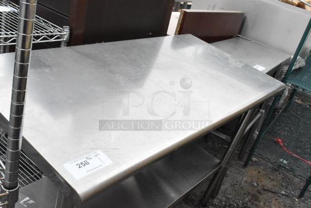 Stainless steel table with under shelf, used condition. Features durable top, visible markings, and attached auction tag.