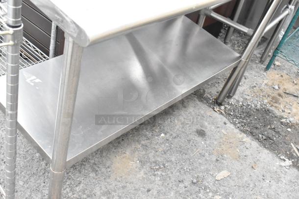 Stainless steel table with under shelf, durable construction, lightly worn. Ideal for kitchen or workshop use.