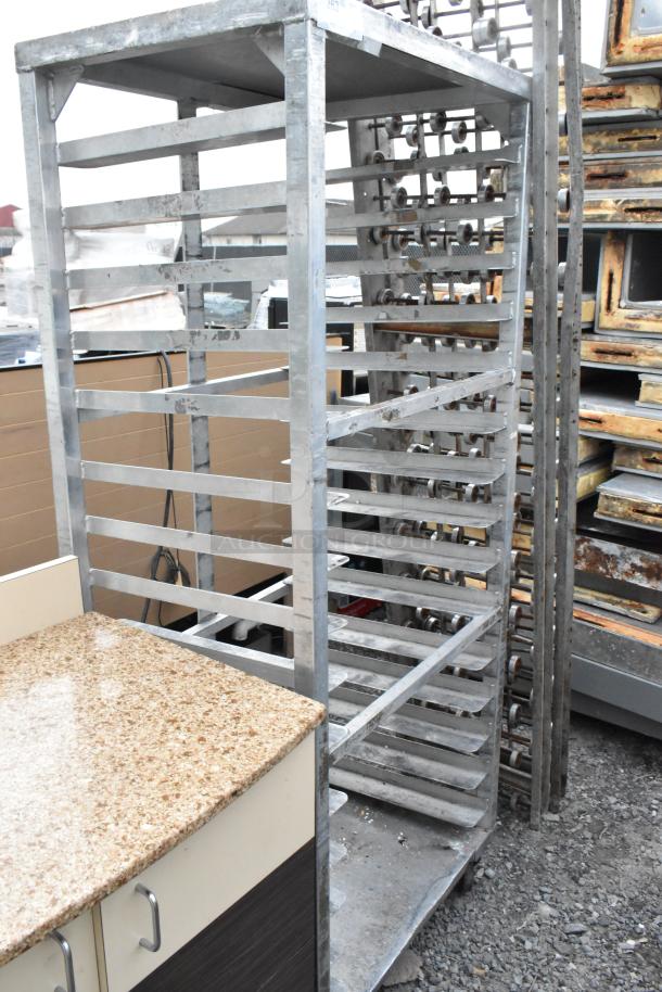 Metal commercial pan transport rack with multiple shelves on heavy-duty casters, showing signs of wear. Ideal for bakery use.