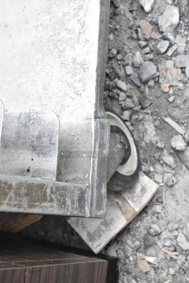 Metal commercial pan transport rack with sturdy commercial casters, metal construction visible, used condition.