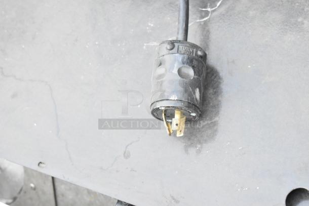 Close-up of a black electrical plug with visible prongs on a textured gray surface.