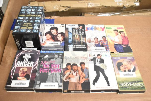 18 assorted VHS tapes including "Jeffrey," "Three Men and a Baby," and "Johnny Carson Collection." Various movie titles; used condition.