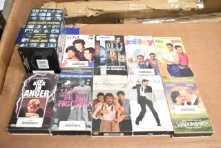 18 assorted VHS tapes including "Jeffrey," "Three Men and a Baby," and "Johnny Carson Collection." Various movie titles; used condition.
