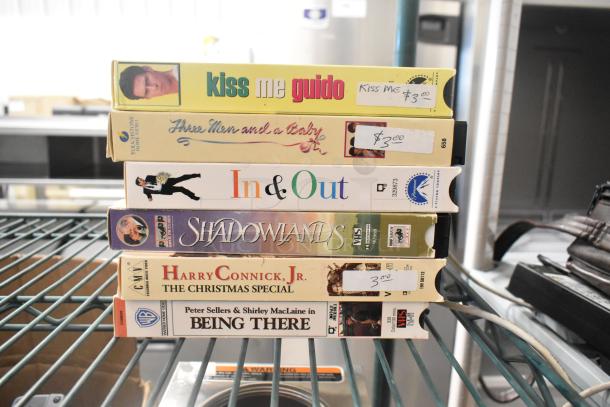 Stack of 7 VHS tapes, including "Three Men and a Baby" and "Shadowlands," each marked with $3 price tags.