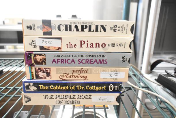 Stack of VHS tapes including "Chaplin," "The Piano," "Africa Screams," "Perfect Harmony," priced labels visible.