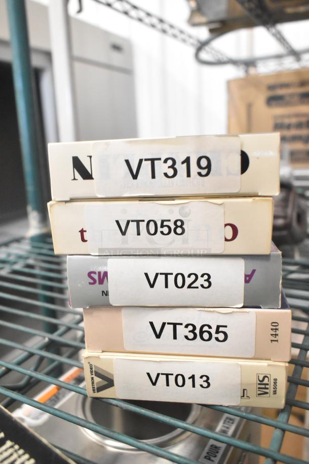 Stack of VHS tapes including Jeffrey, Three Men and a Baby, Johnny Carson Collection. Visible labels: VT319, VT058, VT023.