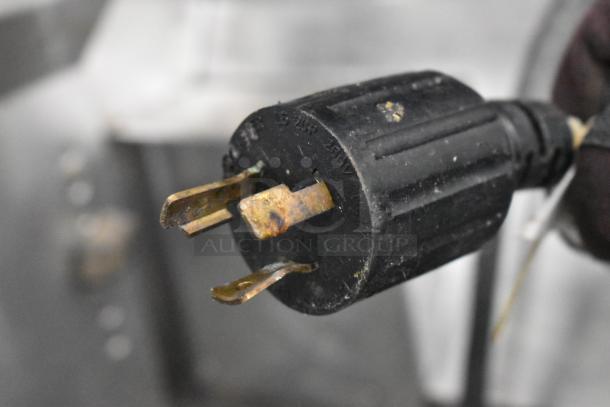 Close-up of a black power plug with two rusted prongs, showing moderate wear. Background is blurred.