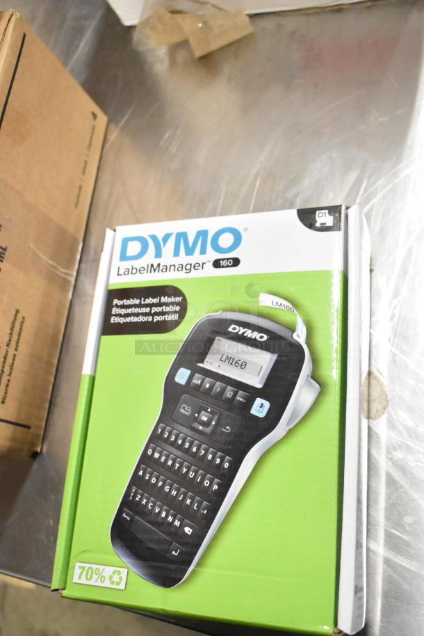Brand new Dymo LabelManager 160 box and Staples computer paper pack; sealed packaging; ideal for office use.