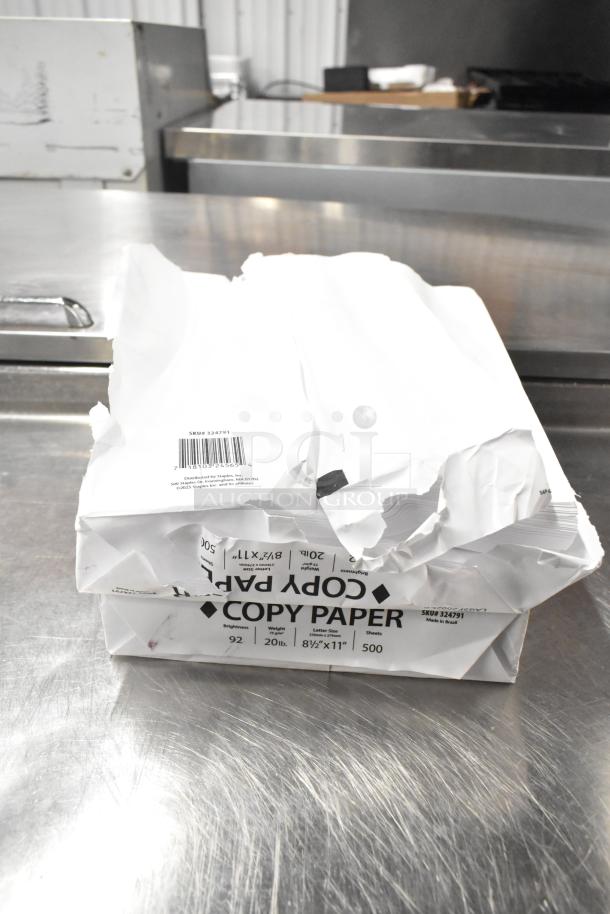 Lot of damaged copy paper reams on metal surface, SKU 324791 visible, part of a 25-item auction lot.