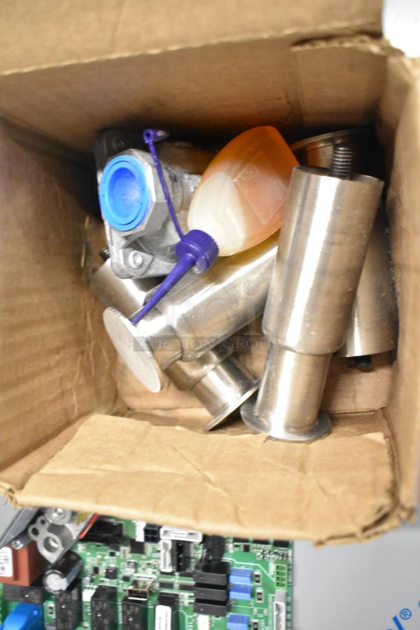 Box containing new items, including Cleveland 105784 Plt Asy;Nat;0.018 Intermittent, metal legs, food-grade lubricating oil.