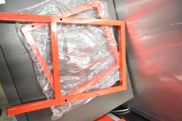 Red metal frame pieces from a new scratch and dent commercial popcorn machine and cart, partially wrapped in plastic.