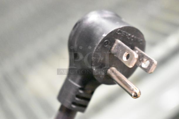 Close-up of a power plug from the 2023 True GDM-26F-HC Commercial Freezer, 115V, 1 Phase, showing metal prongs and black casing.