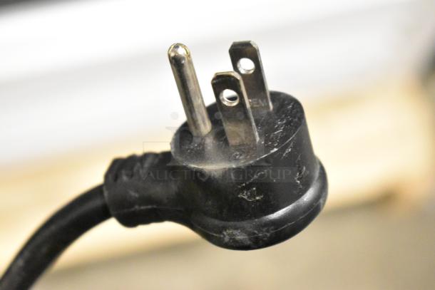 Close-up of a standard three-pronged black electrical plug, slightly worn, likely from a commercial cooler.