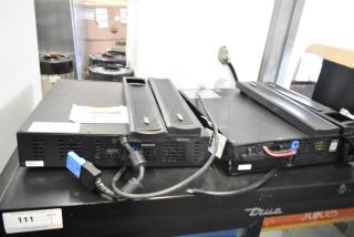 Two APC Uninterruptible Power Supplies, black, with visible cables and APC logo, in good condition.