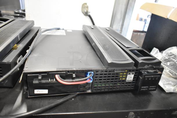 Two APC Uninterruptible Power Supplies, model visible, in good condition. Black casing with connectivity ports and visible wiring.