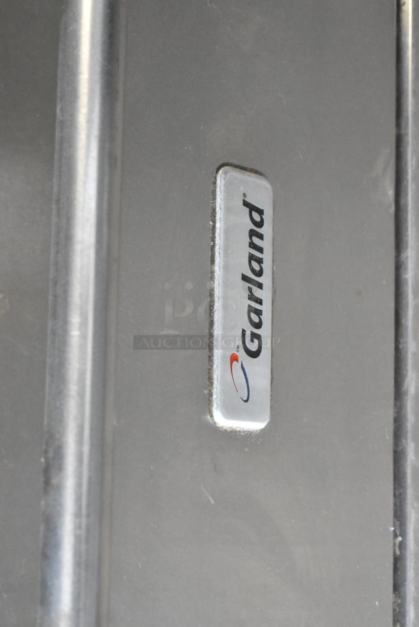 Garland stainless steel gas 6-burner range with oven and backsplash, commercial-grade; features visible logo emblem.