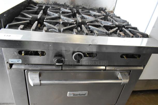Garland stainless steel commercial gas 6-burner range with oven and backsplash. Visible control knobs and brand label. Used condition.