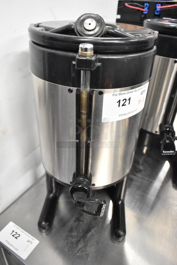 Three Fetco metal countertop beverage dispensers. Features include durable construction, easy-pour spouts, and stable bases. Auction lot label visible.