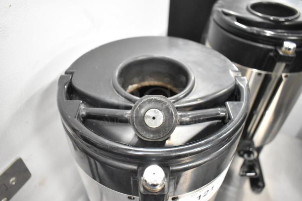 3 Fetco metal countertop beverage dispensers, black lids, stainless steel bodies. Used condition, minor wear visible.