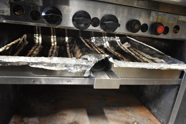 MagiKitch'n stainless steel natural gas charbroiler grill with control knobs, foil-covered cooking grates, in used condition.