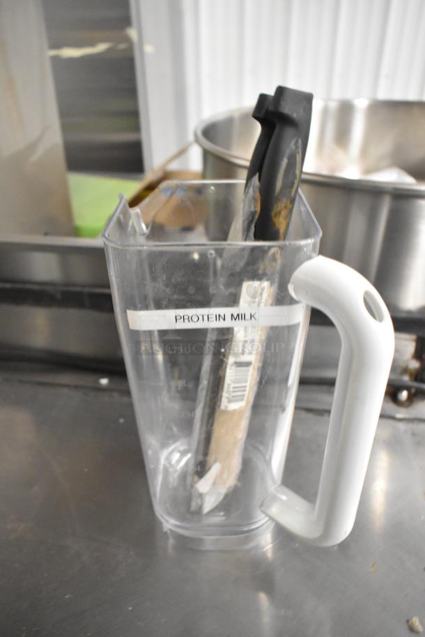 Clear poly pitcher labeled "Protein Milk" containing a knife, part of a six-item auction set with pickup required.