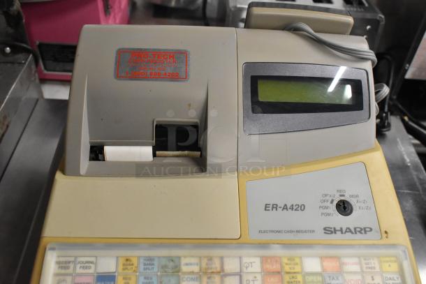 Sharp ER-A420 countertop cash register, beige color. Visible label: "Pro-Tech Cash Register." Features keypad and display screen.