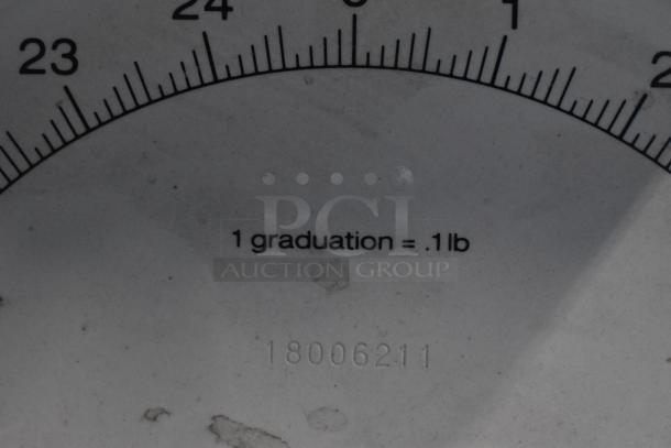 Metal countertop scale face close-up, showing a measurement scale; markings indicate "1 graduation = .1 lb" and number "18006211."