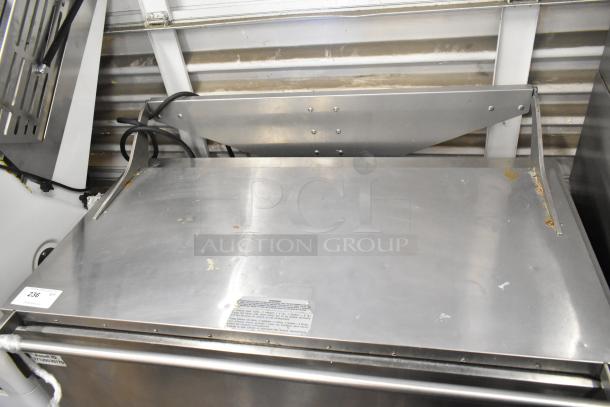 Stainless steel commercial washing/soaking tub with visible wear, scratches, and attached power cord; label with usage instructions.