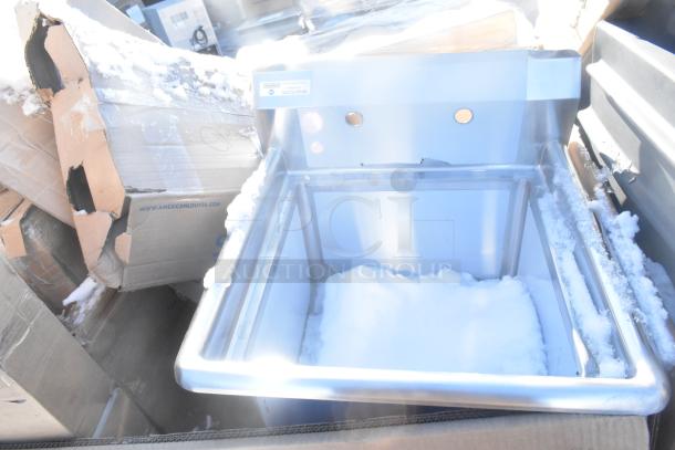 Stainless steel sink with brand label and small dents, surrounded by snow and damaged cardboard boxes.