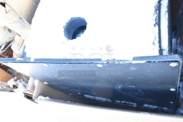 Visible part of a snow-covered item in an auction lot, showing edge of a black surface and round hole. Condition indicated as new.