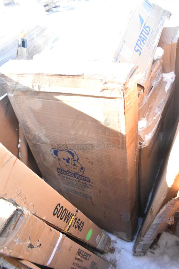 Cardboard boxes labeled "Koala Kare" and "Stratus" containing new scratch and dent items, including shelves and a baby changing station.