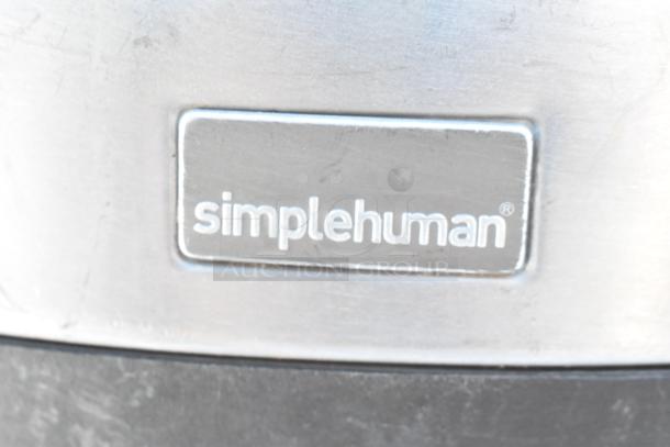 SimpleHuman metal trash can, silver finish, close-up on logo. Visible scratch marks, includes contents.